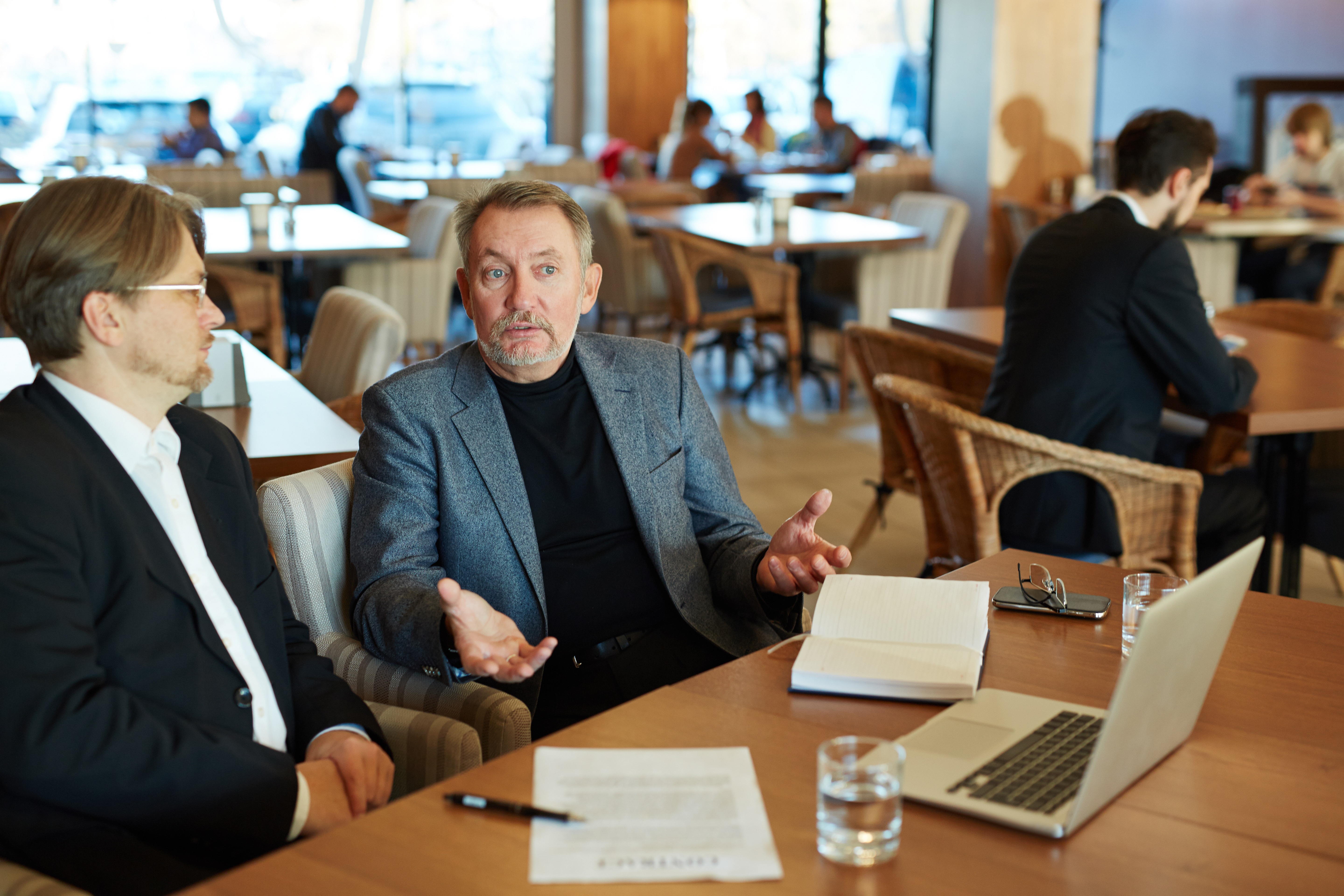 Portrait of mature entrepreneur conducting negotiations with his bearded business partner while sitting in cozy restaurant