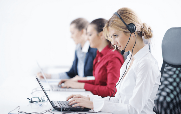 Four customer service representatives wearing headsets working at laptops in an office setting.