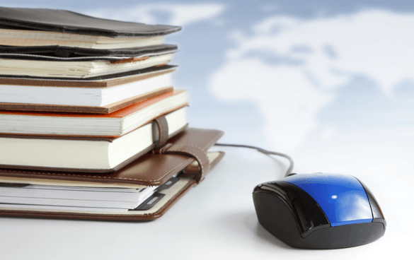 A stack of books and notebooks beside a black and blue computer mouse, with a blurred world map in the background.