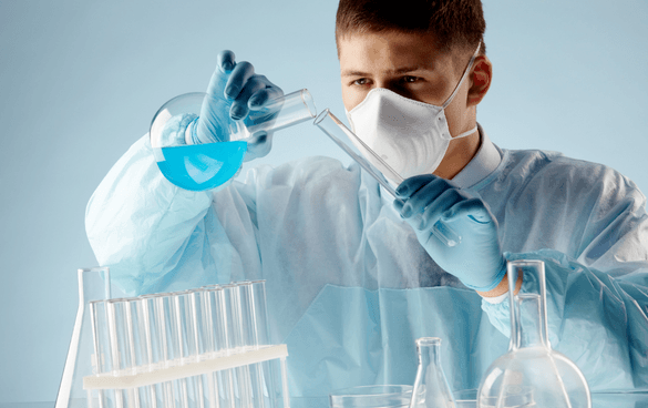 A person in lab attire pouring a blue liquid from a test tube into a flask, surrounded by laboratory equipment.