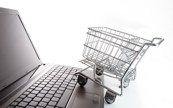 A miniature shopping cart on the right side of an open black laptop keyboard, symbolizing online shopping, on a white surface with a white background.