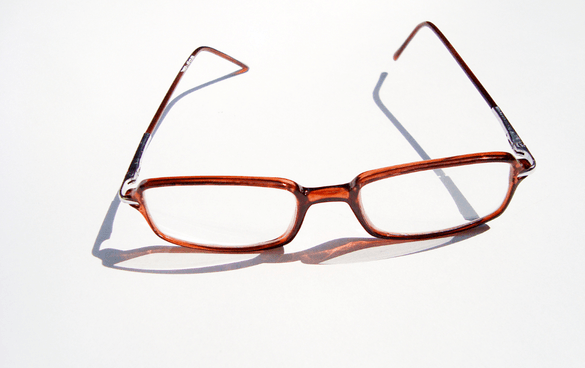 A pair of brown rectangular-framed eyeglasses casting a shadow on a white surface.