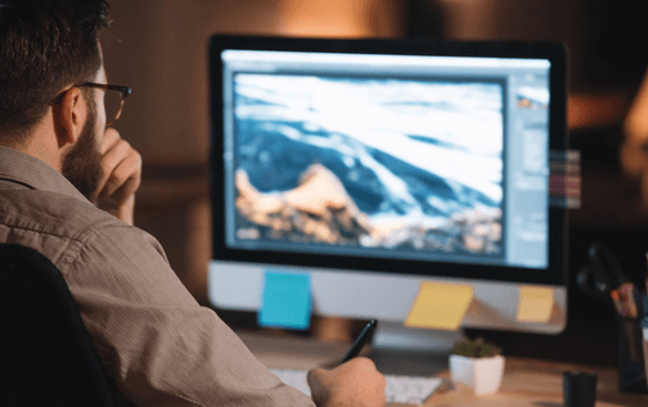 Person working on a computer with a landscape image on the screen, possibly engaged in graphic design or photo editing, in an office environment.