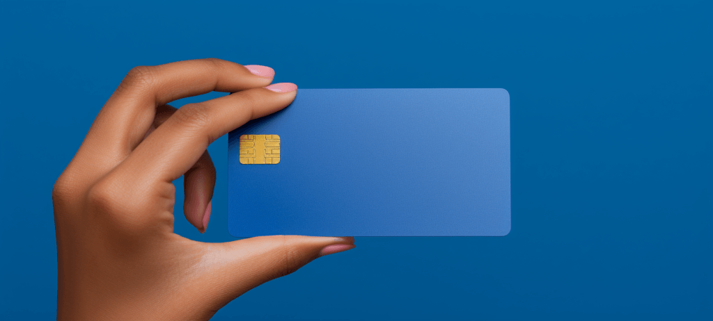 A person's hand with light pink nail polish holding a blue credit card with a gold chip, against a matching blue background.