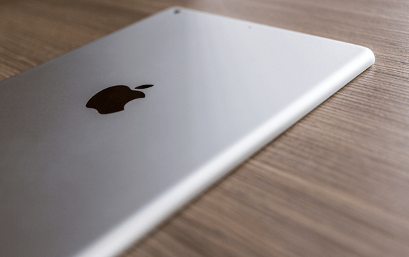 Close-up of the back of a silver tablet with an apple logo, resting on a wooden surface.