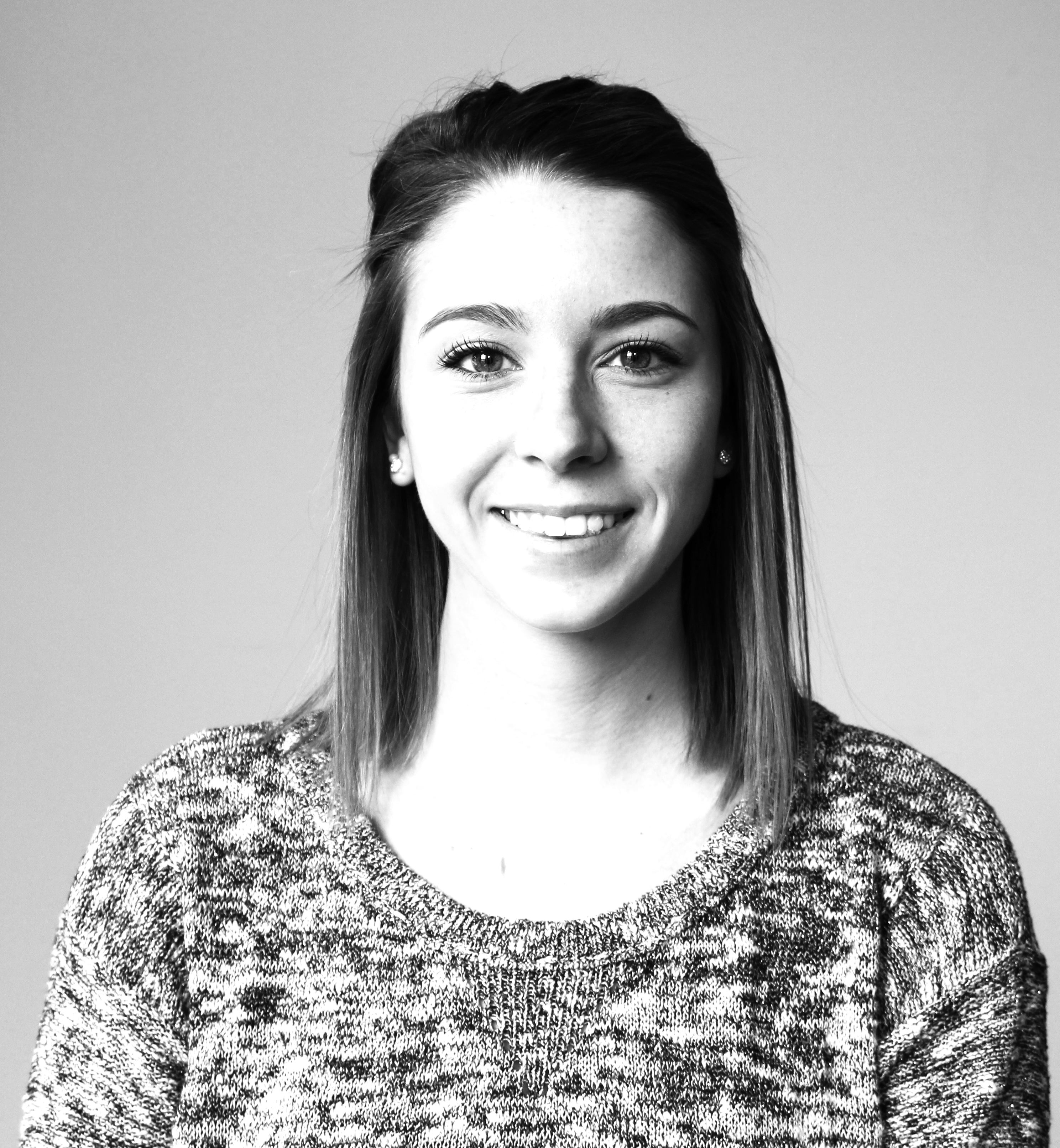 Black and white portrait of a smiling young woman with long straight hair wearing a knitted sweater.