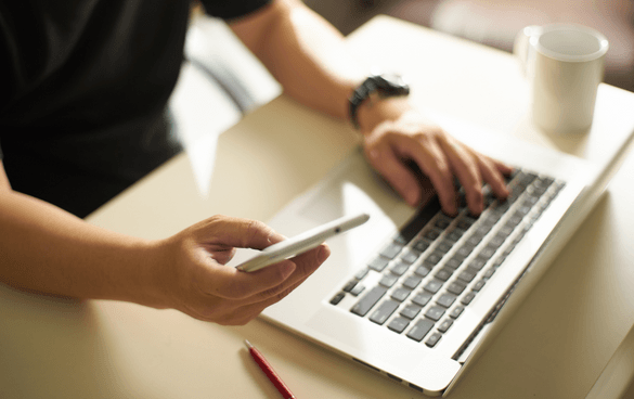 Man typing on a laptop while also holding his phone and browsing