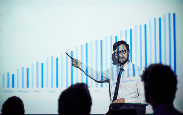 A man presenting a monthly data bar chart to an audience, using a pointer to highlight specific information.