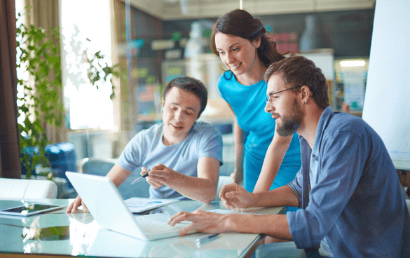 Two young male workers and one female worker standing around a laptop and having a conversation