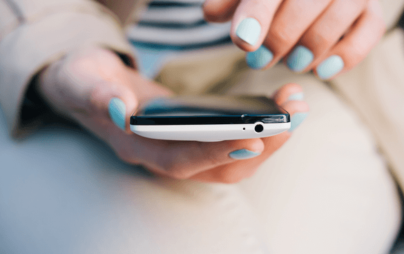 Close-up of a person's hands with light blue nail polish holding a white smartphone, poised to use the touchscreen.