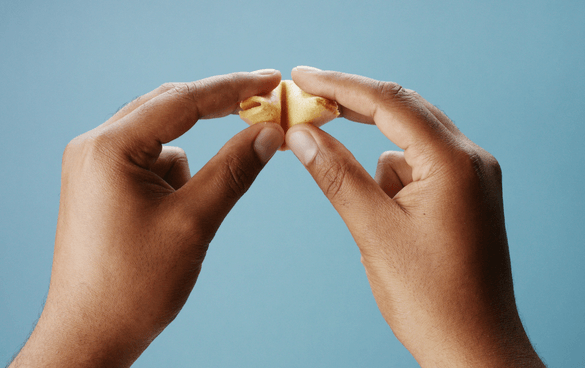 Two hands about to crack open a golden fortune cookie against a blue background.