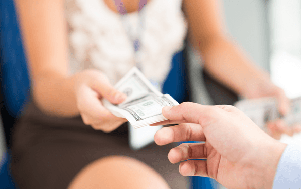 Close-up of a person receiving a stack of US dollar bills from another person, with the recipient wearing a patterned blouse and a lanyard.