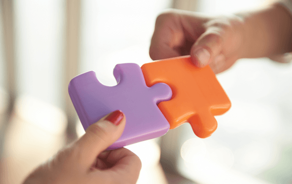 Two hands holding oversized purple and orange puzzle pieces about to interlock.