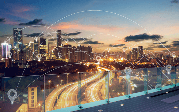 Twilight cityscape with illuminated skyscrapers and a busy highway, overlaid with a graphic representation of a smart city network with lines and nodes.