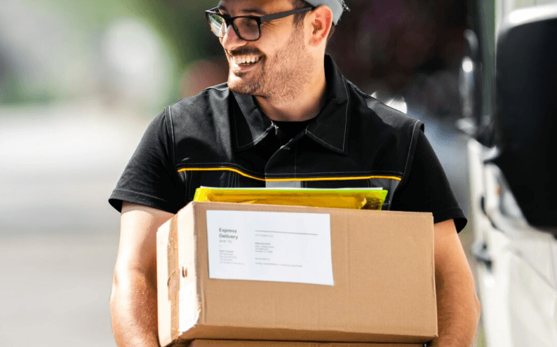 Smiling delivery man in glasses and a black shirt with yellow trim carrying a cardboard box and a yellow envelope labeled 'Express Delivery'.