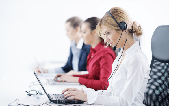 Three women wearing headsets working at laptops in a professional setting, likely a call center or customer service department.