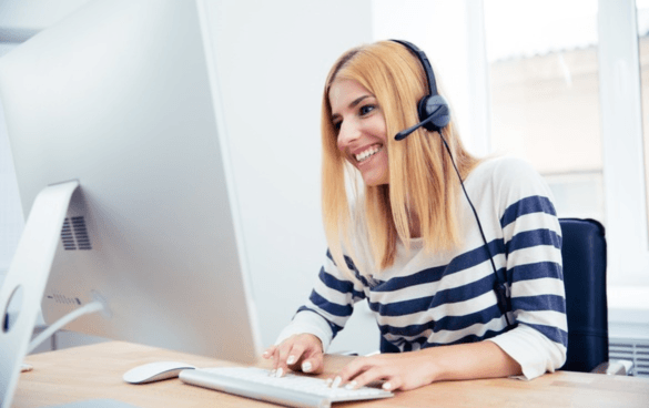 A smiling woman with a headset working at a computer in an office setting.