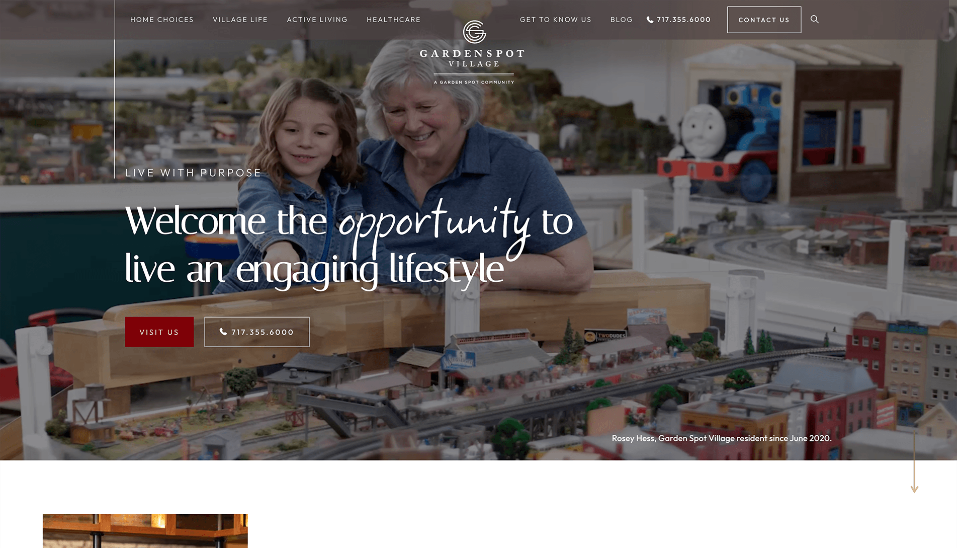 An older woman and a young girl smiling while engaging with a detailed model train set, with promotional text for Garden Spot Village.