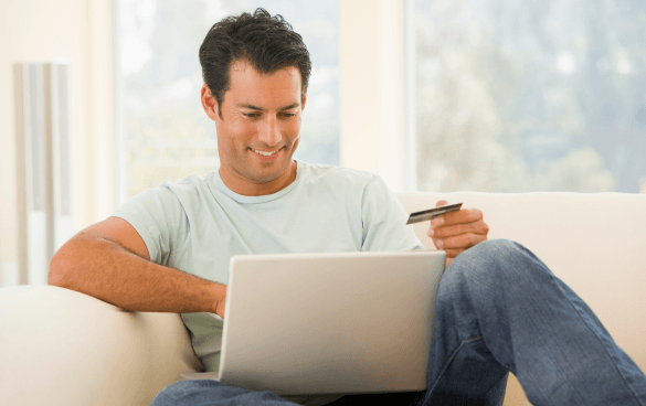 Man sitting on a couch with a laptop and holding up a credit card