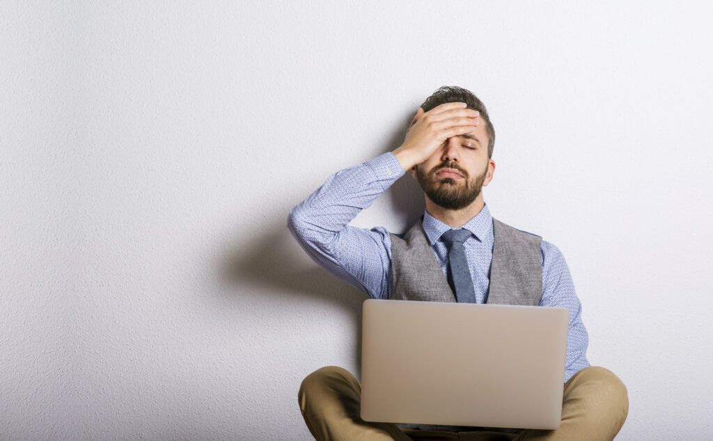 Studio shot of tired hipster businessman working on laptop