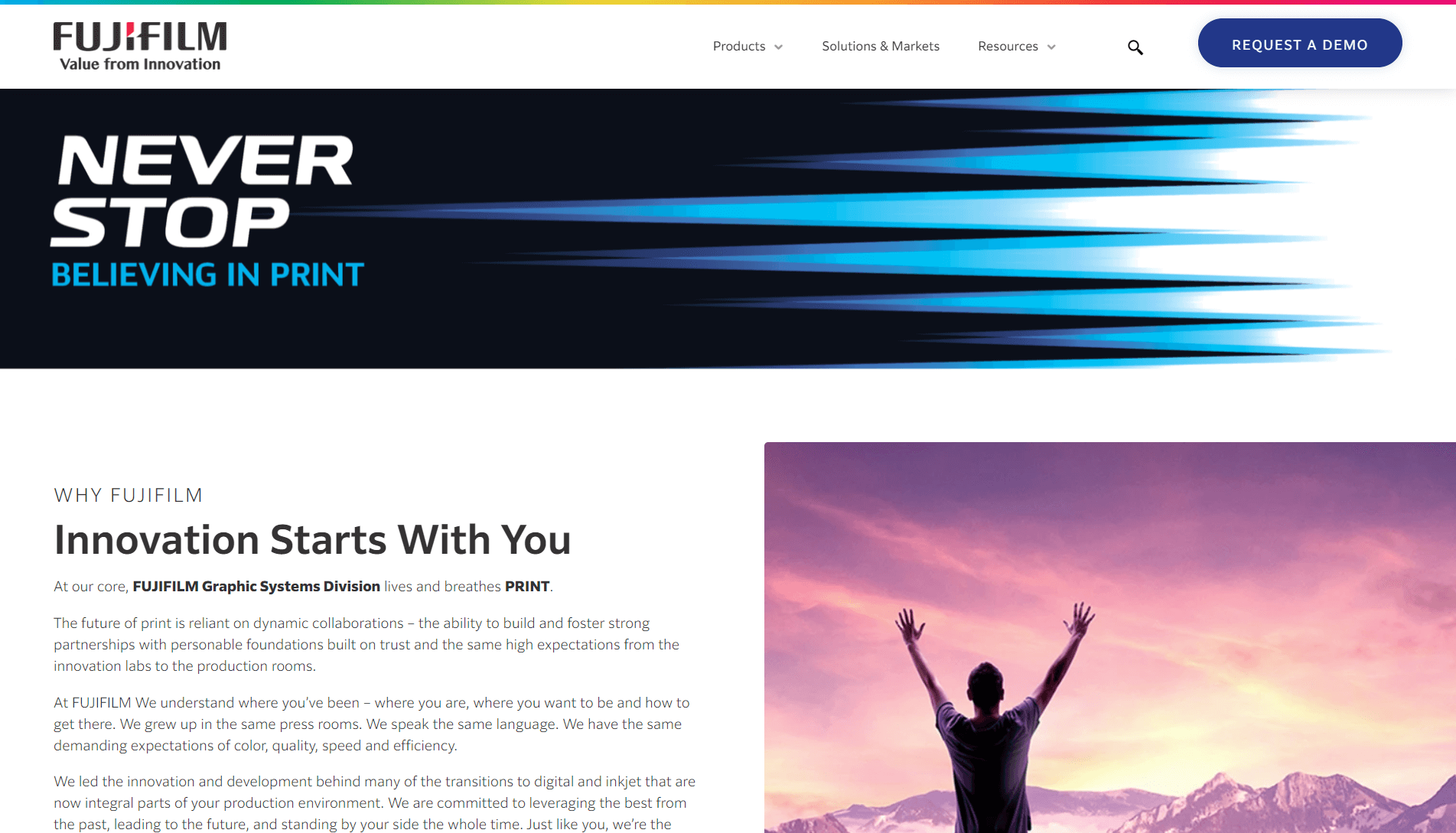 FUJIFILM promotional banner with logo and slogan 'NEVER STOP BELIEVING IN PRINT', followed by a section titled 'WHY FUJIFILM' with descriptive text about their Graphic Systems Division, and a photo of a person with arms raised towards a purple sky over mountains.