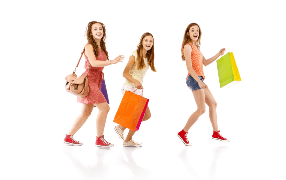 Three young women in casual attire and red sneakers, smiling and walking with colorful shopping bags, against a white background.