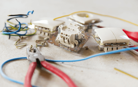 Disassembled electrical switch or socket components with wires, screws, and wire cutters on a light-colored work surface.