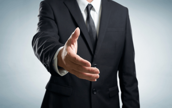 A person in a business suit offering a handshake with the focus on the extended hand against a neutral background.