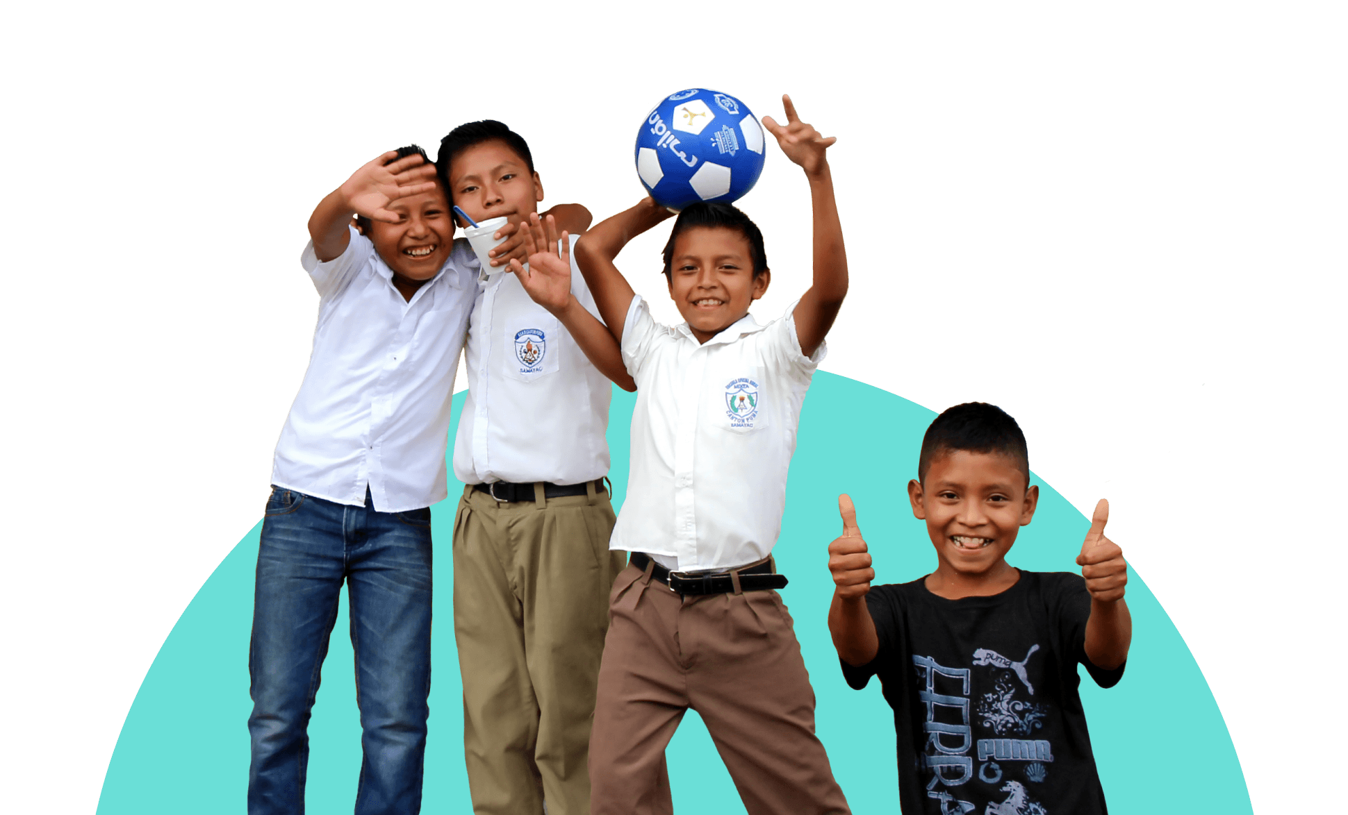 Four cheerful boys posing for the camera, three in school uniforms with one holding a soccer ball, and one in a black t-shirt giving a thumbs-up.