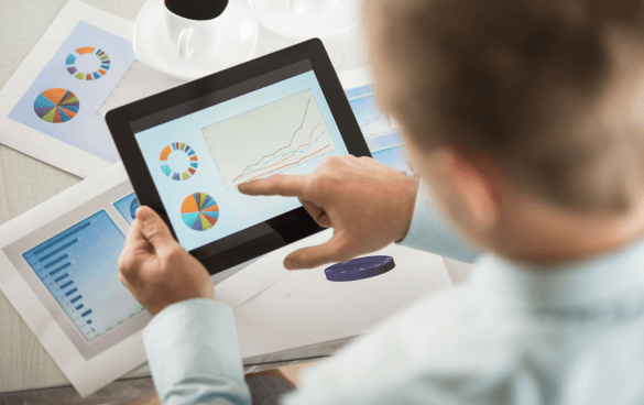 Person reviewing a line graph and pie charts on a tablet with printed charts and a cup of coffee on the table.