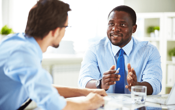 Two professionals in a meeting, one is speaking and gesturing while the other listens attentively.