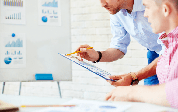 Two professionals reviewing a document with charts and graphs in the background, indicating a business or project discussion.