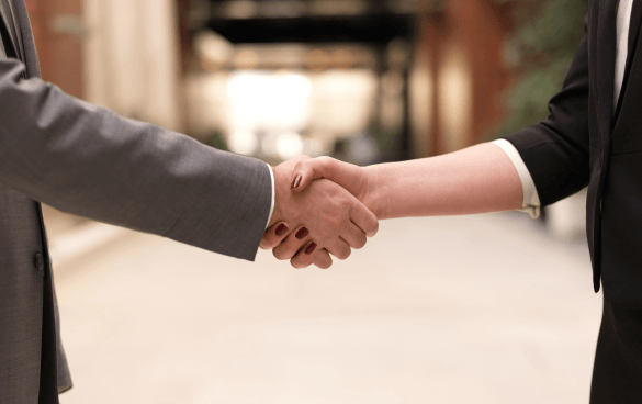 Two individuals in business attire shaking hands, with a blurred indoor background.