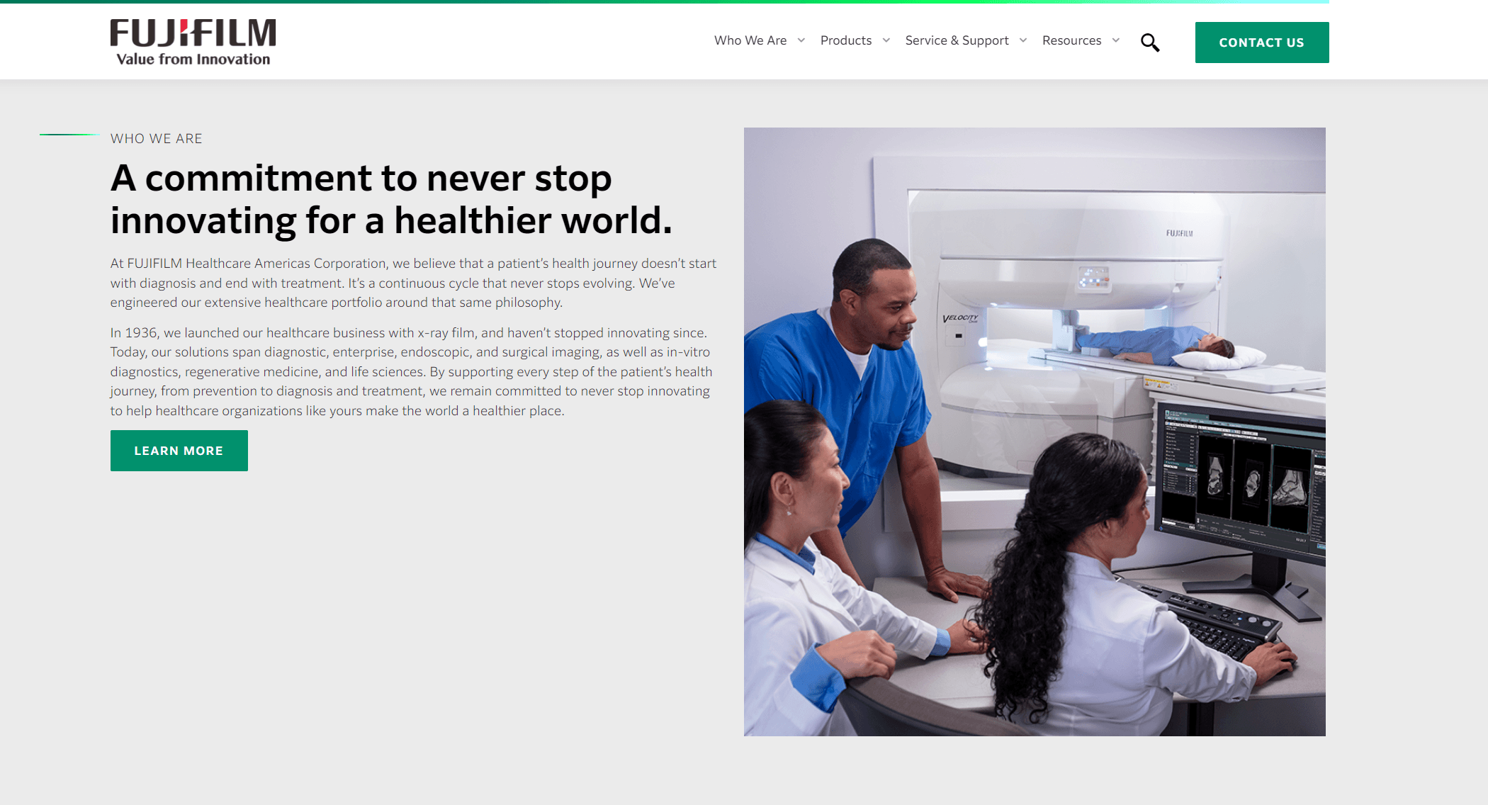 Three healthcare professionals operating and monitoring medical imaging equipment with a patient undergoing a scan in a FUJIFILM medical imaging suite.