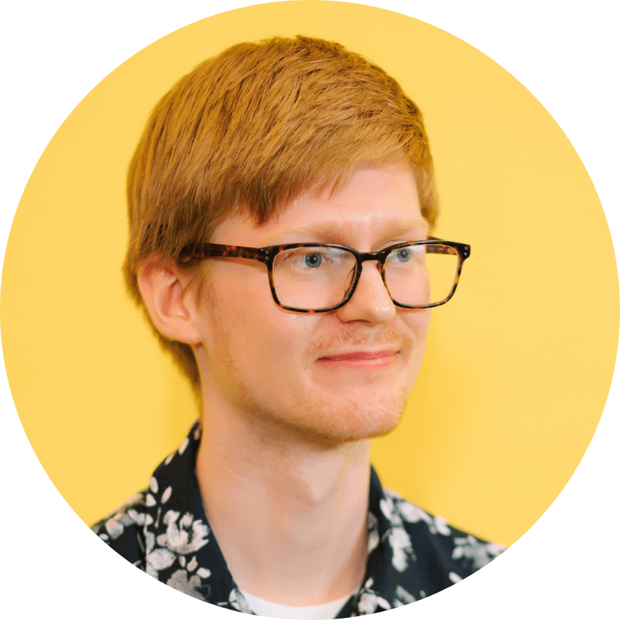 A smiling person with short blond hair wearing glasses and a floral shirt against a yellow background.