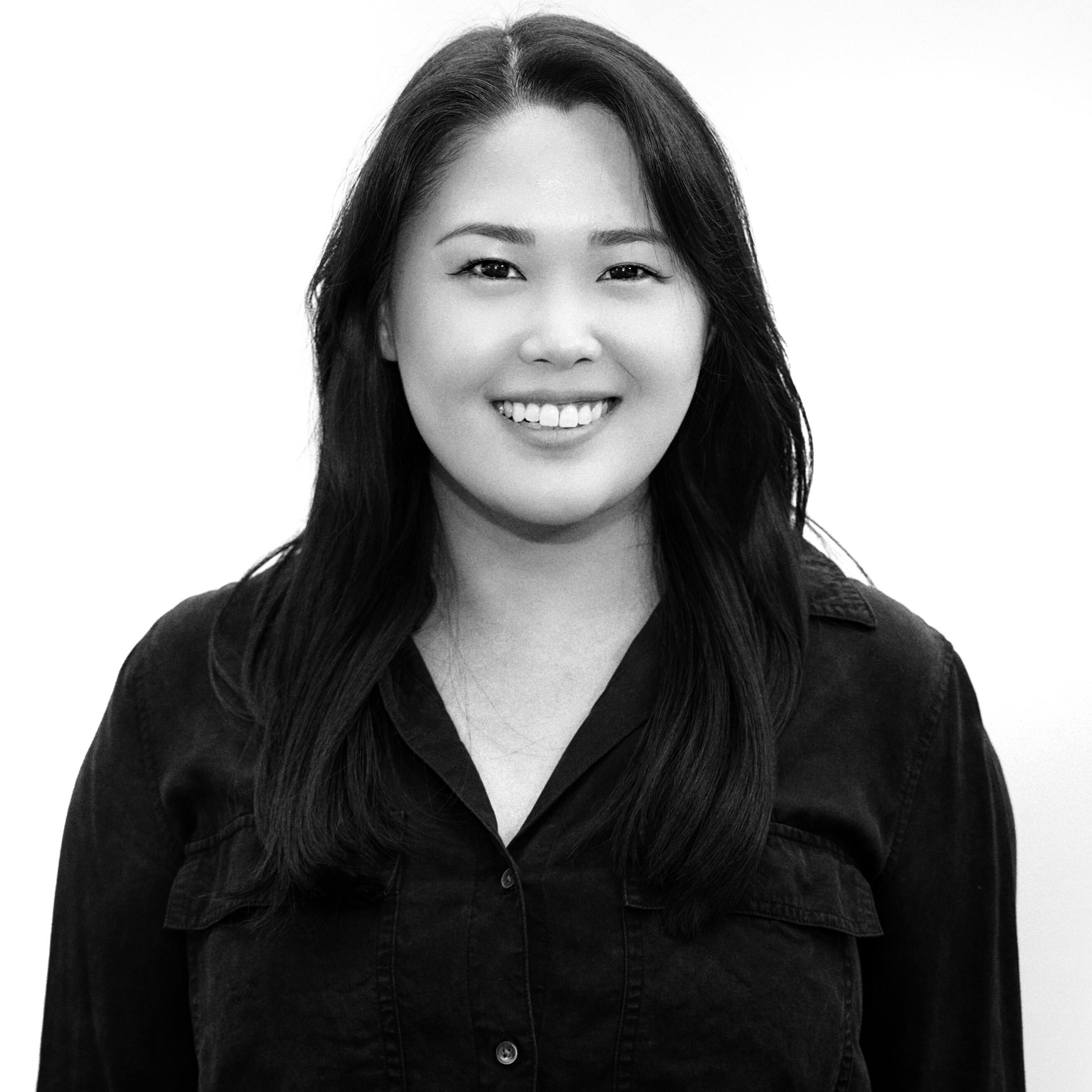 Black and white portrait of a smiling woman with long hair wearing a dark shirt.