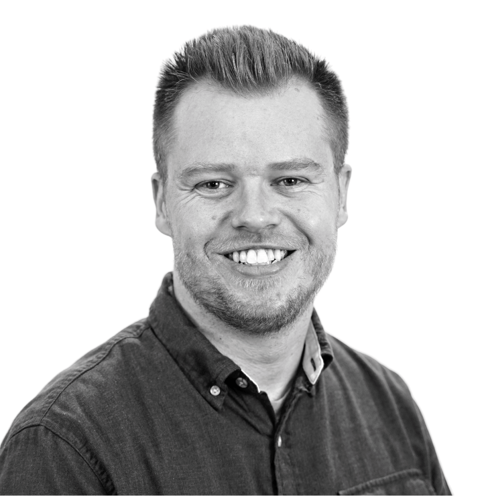 Black and white portrait of a smiling man with short hair and a beard, wearing a button-up shirt.