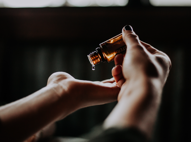 A person's hands with one hand holding an amber dropper bottle dispensing a liquid drop into the other hand.