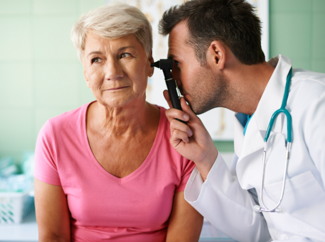 A doctor examining the ear of an elderly female patient with an otoscope in a medical office.