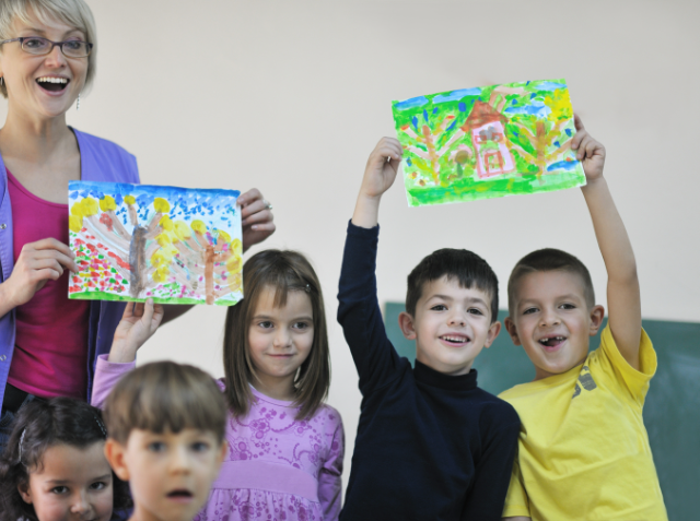 A teacher and young children proudly displaying their colorful paintings in a classroom.