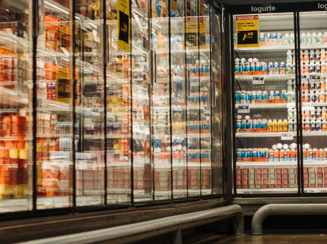 Refrigerated supermarket aisle with glass doors displaying an assortment of dairy products, including milk and yogurt, with visible price tags.