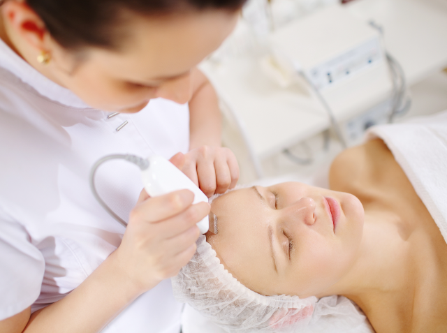 A skincare professional administering a facial treatment using a handheld device on a relaxed woman in a beauty clinic.