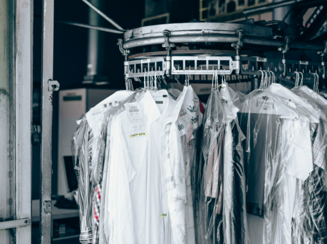 A conveyor with clothes on hangers covered in clear plastic garment bags, indicative of a dry cleaning business.