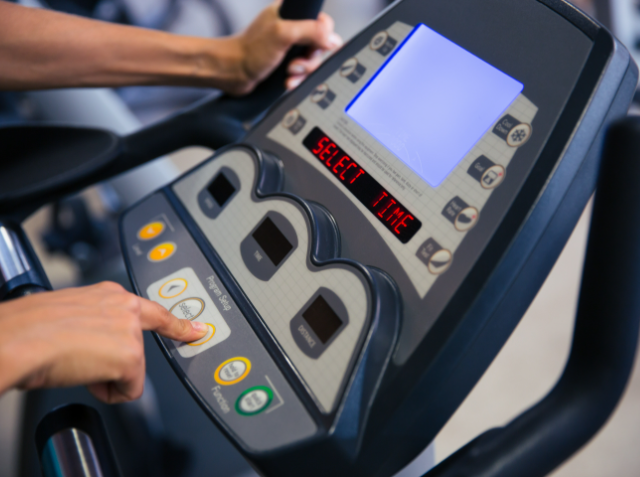 A person's hand is pressing a button on a treadmill console, which displays the word 'TIME' in red, alongside other control buttons.