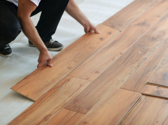 Person installing laminate wood flooring, kneeling and placing a plank to continue the pattern.