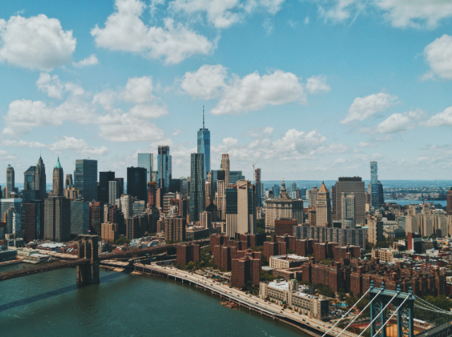 Aerial view of a city skyline with a prominent skyscraper, a river with a bridge, and surrounding high-rise buildings on a clear day.