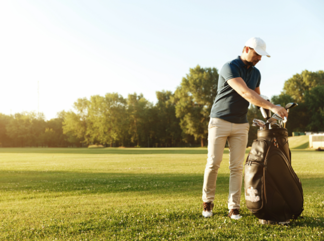 A man in golf attire selecting a club from his bag on a sunny golf course.