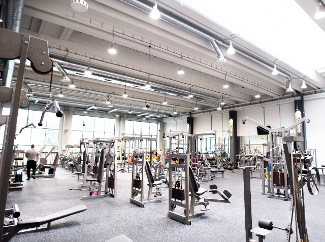 A modern gym with a variety of exercise equipment including weight machines, free weights, and cardio machines, with individuals working out.