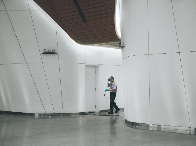 A cleaner mopping the floor in a modern building with curved white walls and a wooden ceiling.