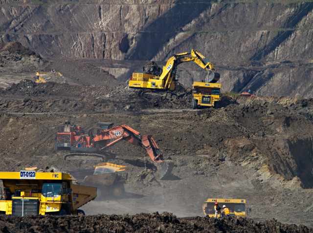 Open-pit mining operation with heavy machinery including excavators and dump trucks working in a large terraced pit.